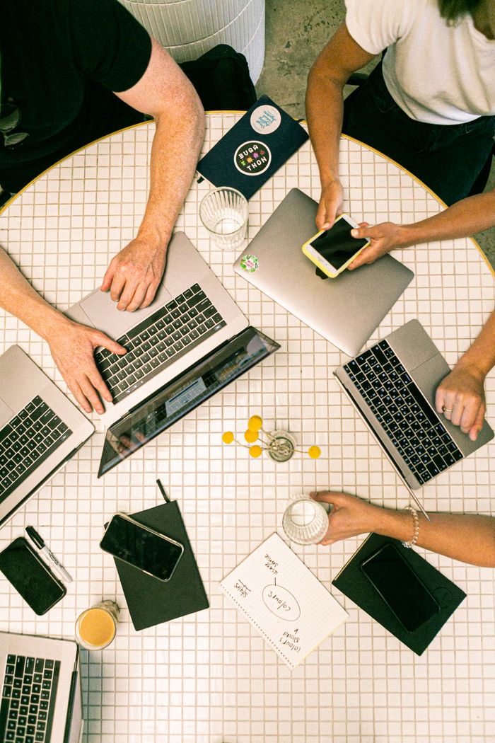 About Top view of a team collaborating with laptops, phones, and notes in a modern office.