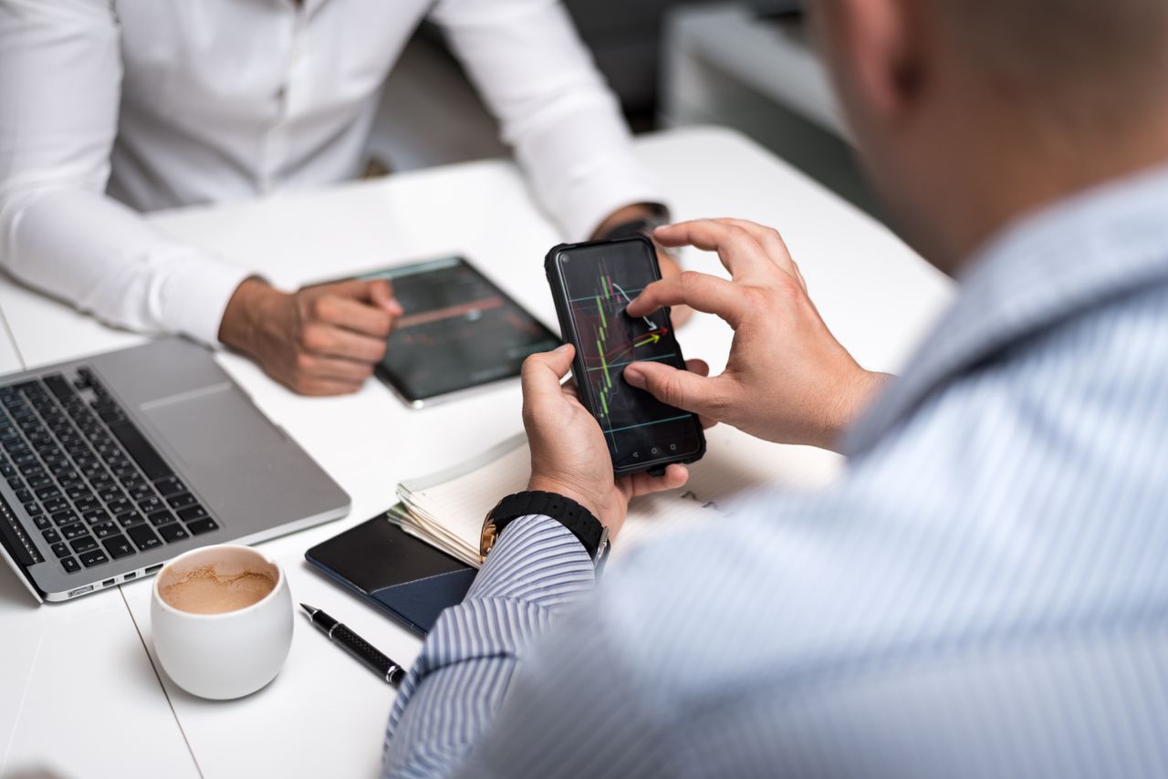 Portfolio Business professionals using smartphones and tablets to analyze trading charts during a meeting.