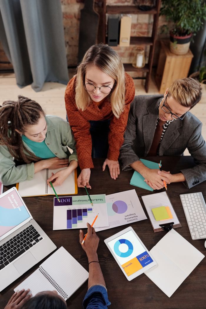 About Top view of a diverse group discussing business reports and charts around a desk.