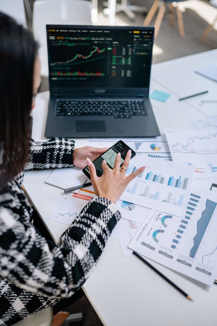 Offerings Businesswoman evaluating stock market trends using graphs and smartphone in office.
