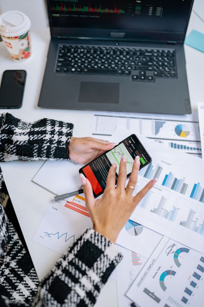 Portfolio Person analyzing business charts with smartphone and laptop on desk.